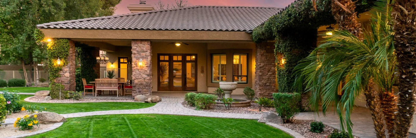 A large landscaped property at dusk with lawn, planting beds and mature trees